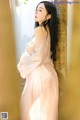 A woman in a pink dress leaning against a wall.