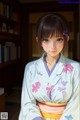 A woman in a kimono standing in front of a bookshelf.