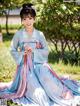 A woman in a blue and pink hanbok sitting in the grass.