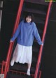 A woman in a blue sweater and white skirt standing on a set of stairs.