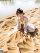 A woman in a white dress sitting on a sandy beach.