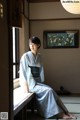 A woman in a blue kimono sitting on a window sill.