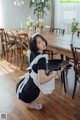 A woman in a maid outfit crouching on the floor in front of a dining room table.