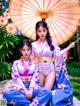 Two young women in kimonos sitting under an umbrella.